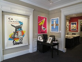 Posters of varied sizes decorate wall of gallery; beige, white, red, blue