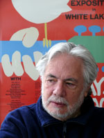Man in front of poster with guitar, hand, and dove; white, blue, red