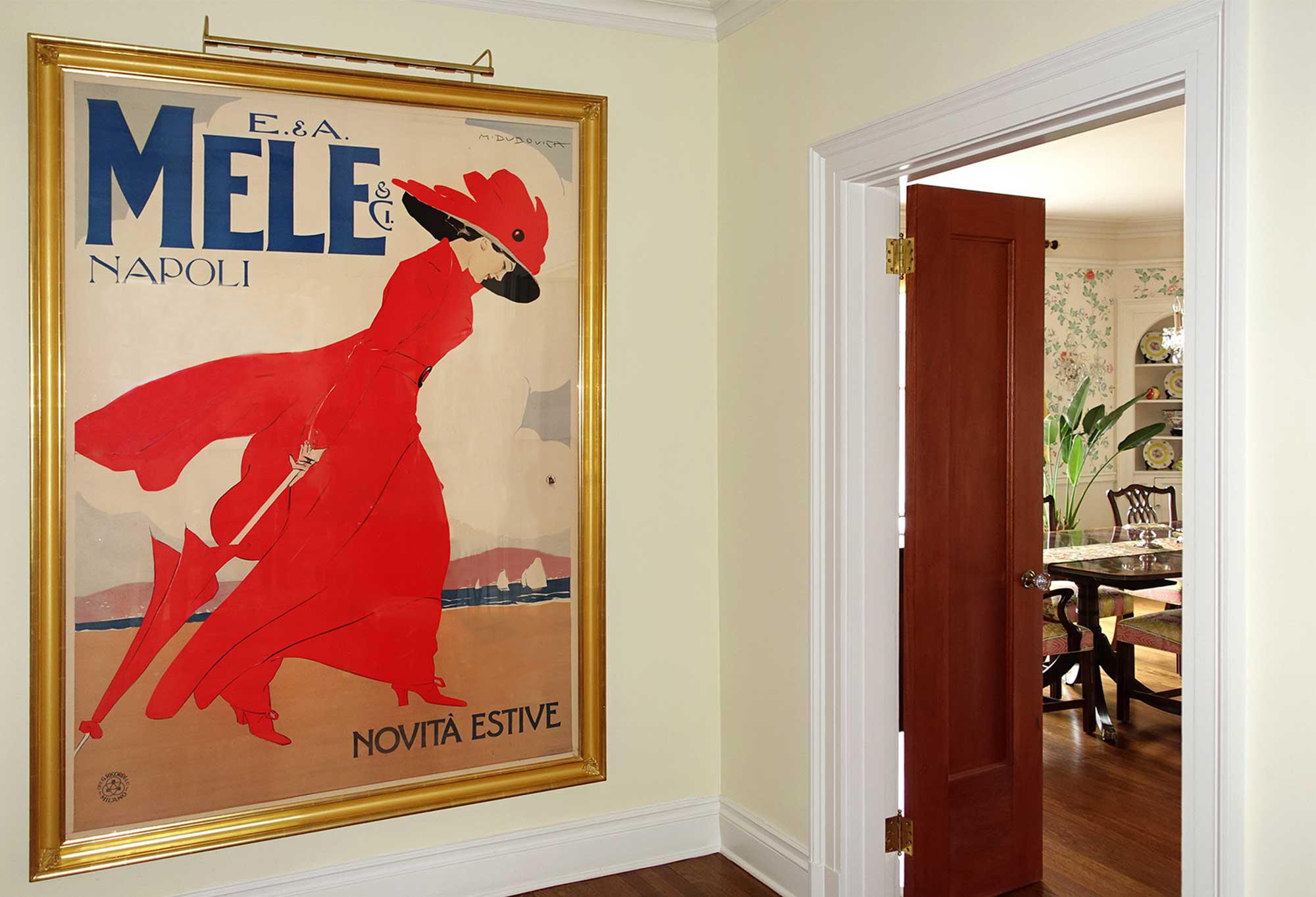 framed poster of woman in red dress and hat next to open door; red, gold, brown