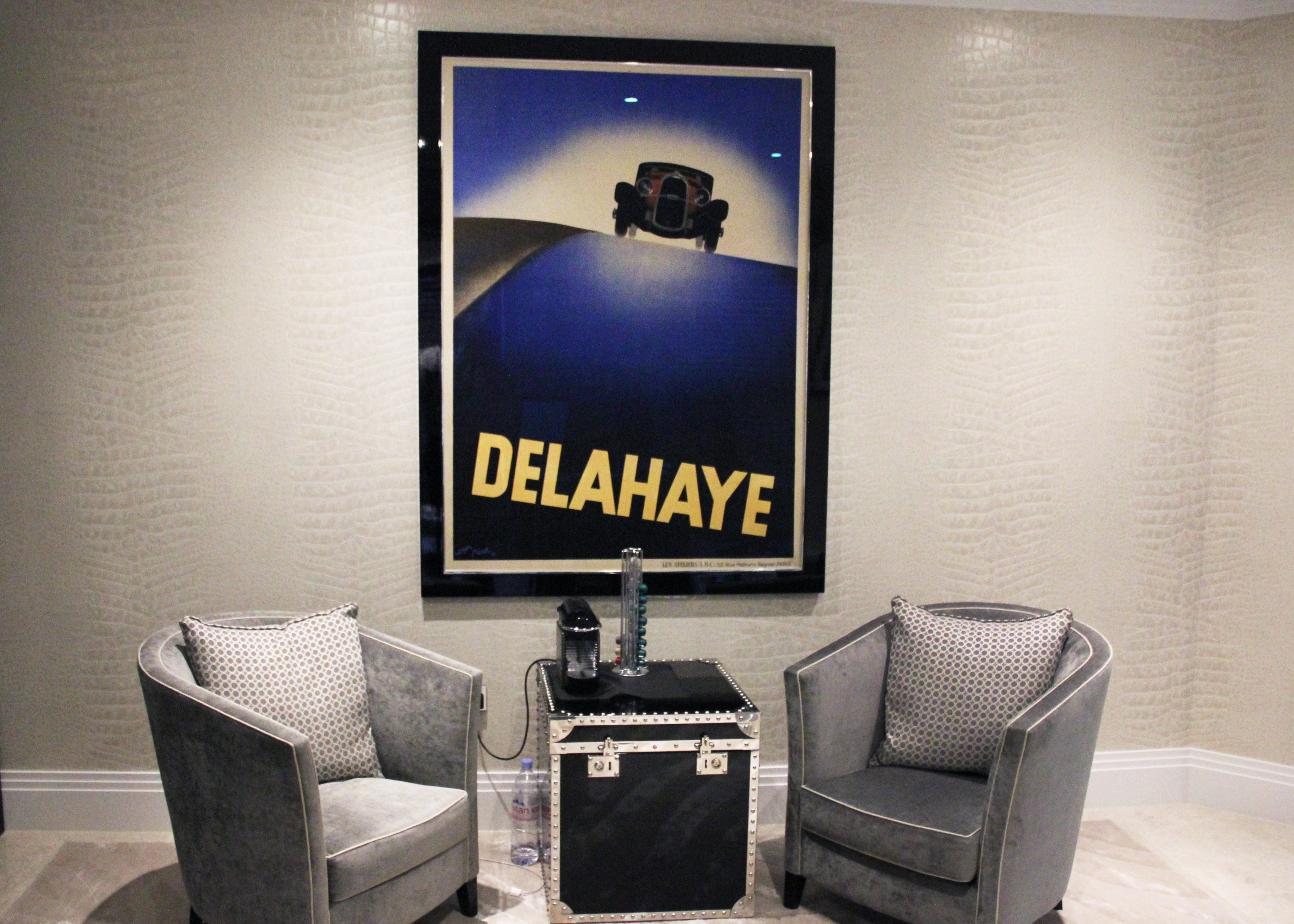 framed art deco car poster on wall behind two armchairs; blue, grey, black